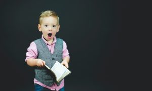 boy wearing gray vest and pink dress shirt holding book