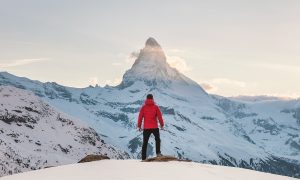 person in red hoodie standing on snowy mountain during daytime