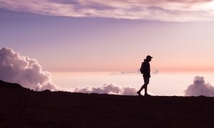 silhouette of person walking under white clouds