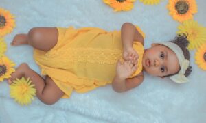 baby in yellow dress lying on white textile