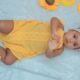 baby in yellow dress lying on white textile