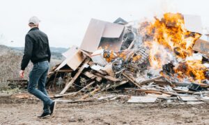 man in black jacket and blue denim jeans standing in front of bonfire