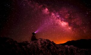 silhouette photo of person holding flashlight under milk way