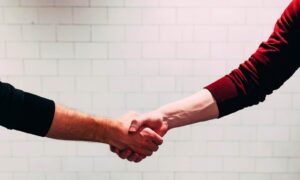 two person shaking hands near white painted wall