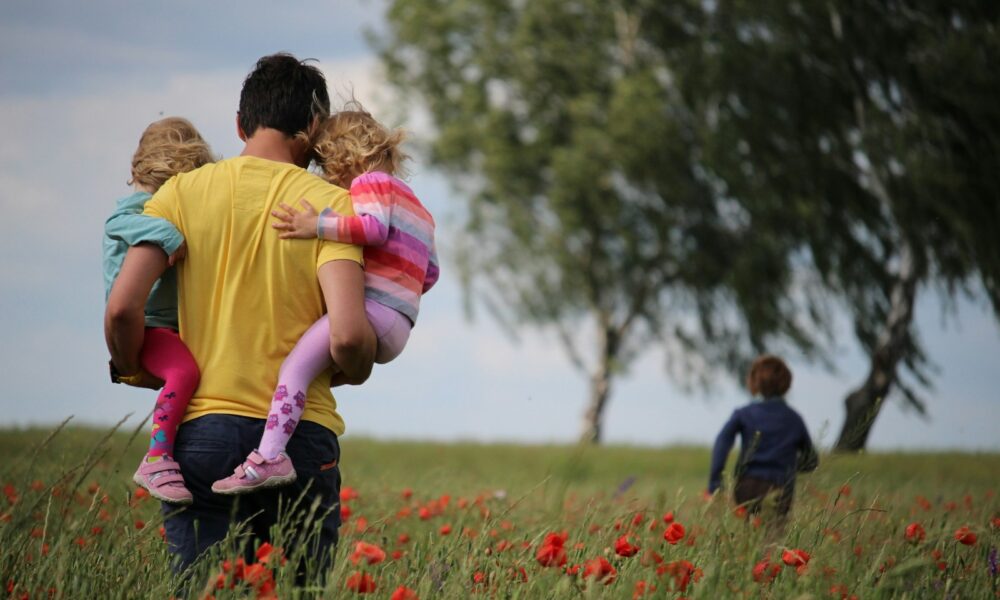 man carrying to girls on field of red petaled flower